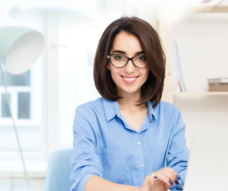 pretty girl in blue shirt sitting in the office with a smile working with laptop